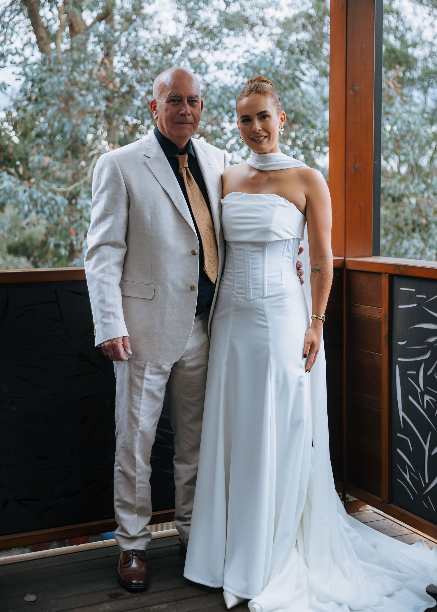 Bride in elegant white strapless gown with halter detail poses with older gentleman in cream suit.