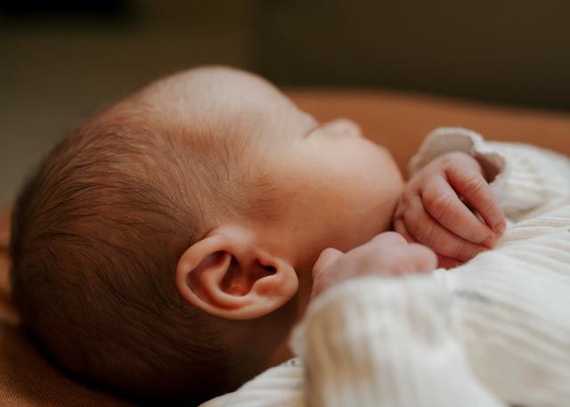 Close-up side profile of sleeping newborn baby with delicate features resting on soft cushion.