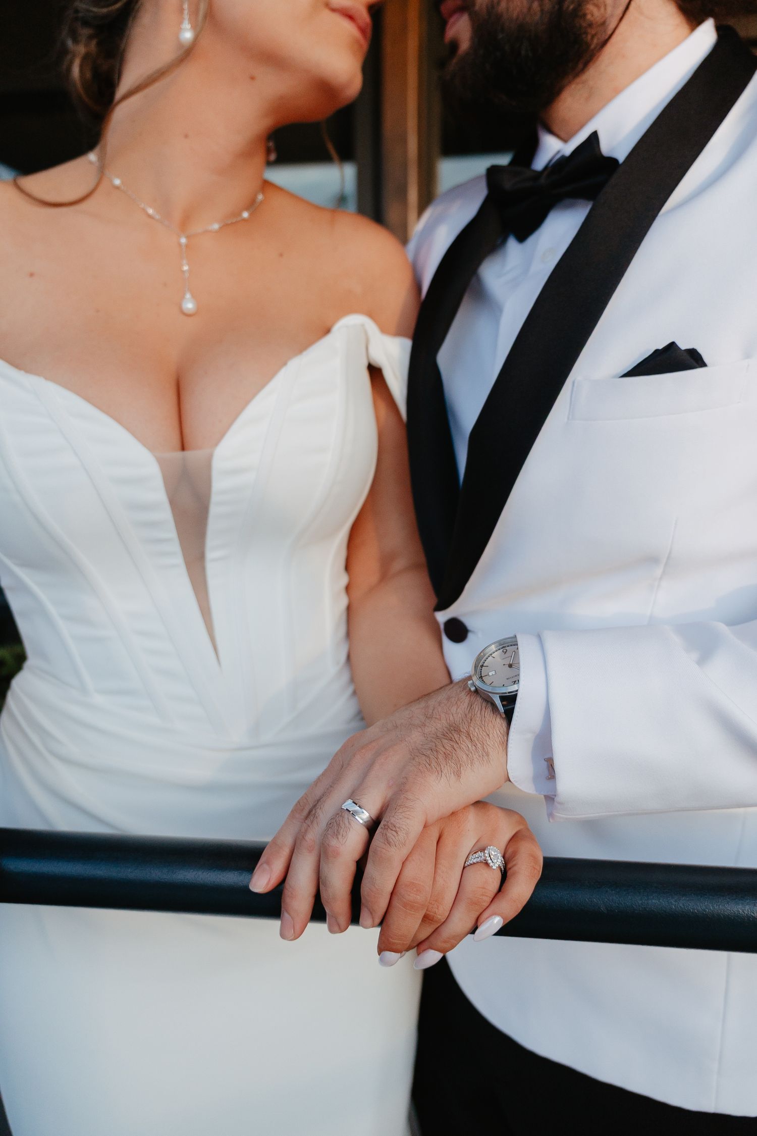 Close-up of bride and groom showing wedding rings while standing together at outdoor railing.