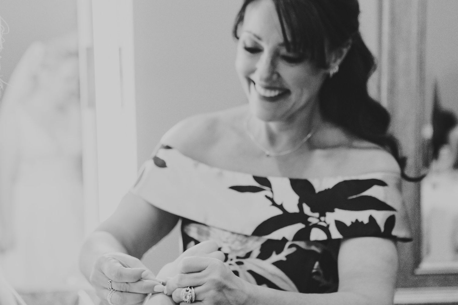 Black and white photo of a smiling bride in floral off-shoulder dress holding a newborn baby.