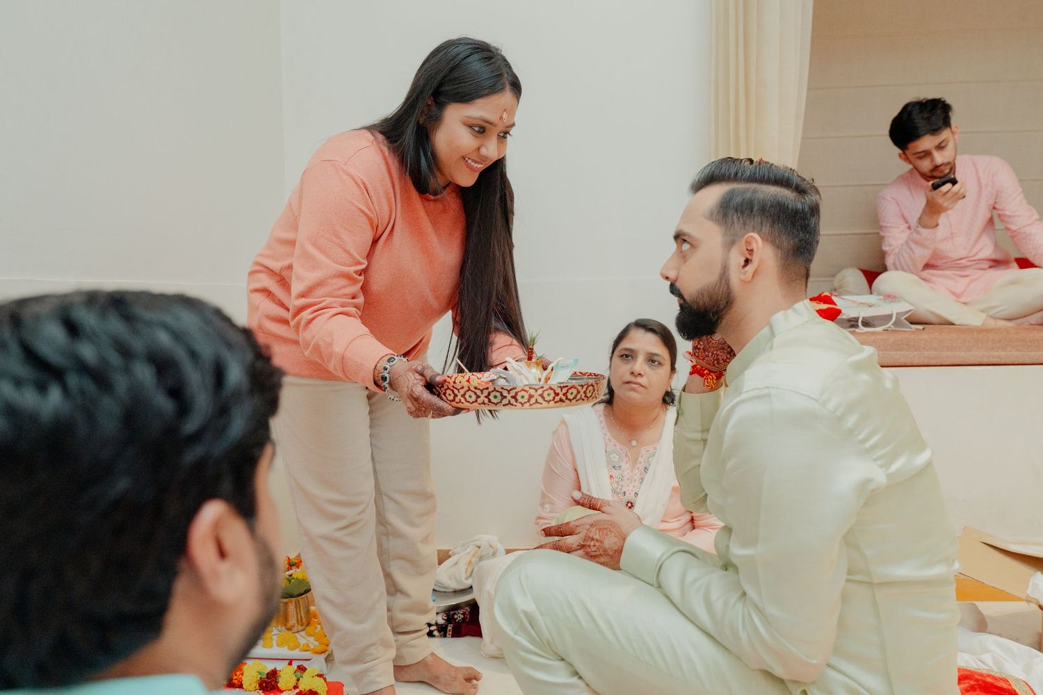 Woman presenting a decorative tray to a man during an Indian Raksha Bandhan ceremony indoors.