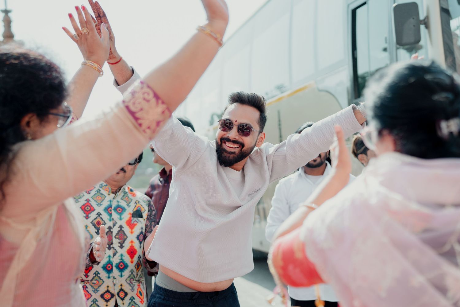 A joyful man in sunglasses dancing with raised hands at a colorful outdoor celebration.
