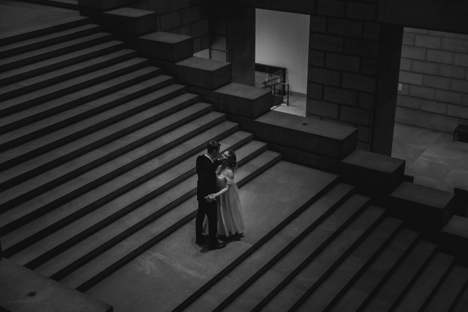 Black and white dramatic photo of a couple embracing on monumental stone steps in dim light. Philadelphia Art Museum Photographer.