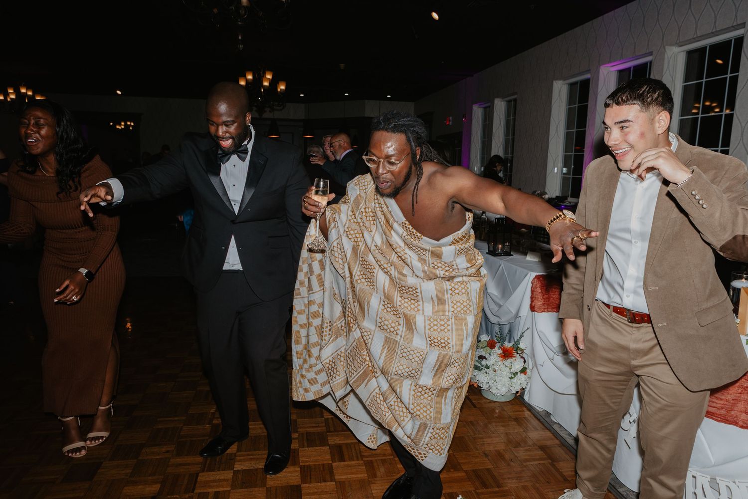 Guests dancing joyfully at a wedding reception, wearing formal attire including a plaid wrap dress and tan suit in Eastern PA
