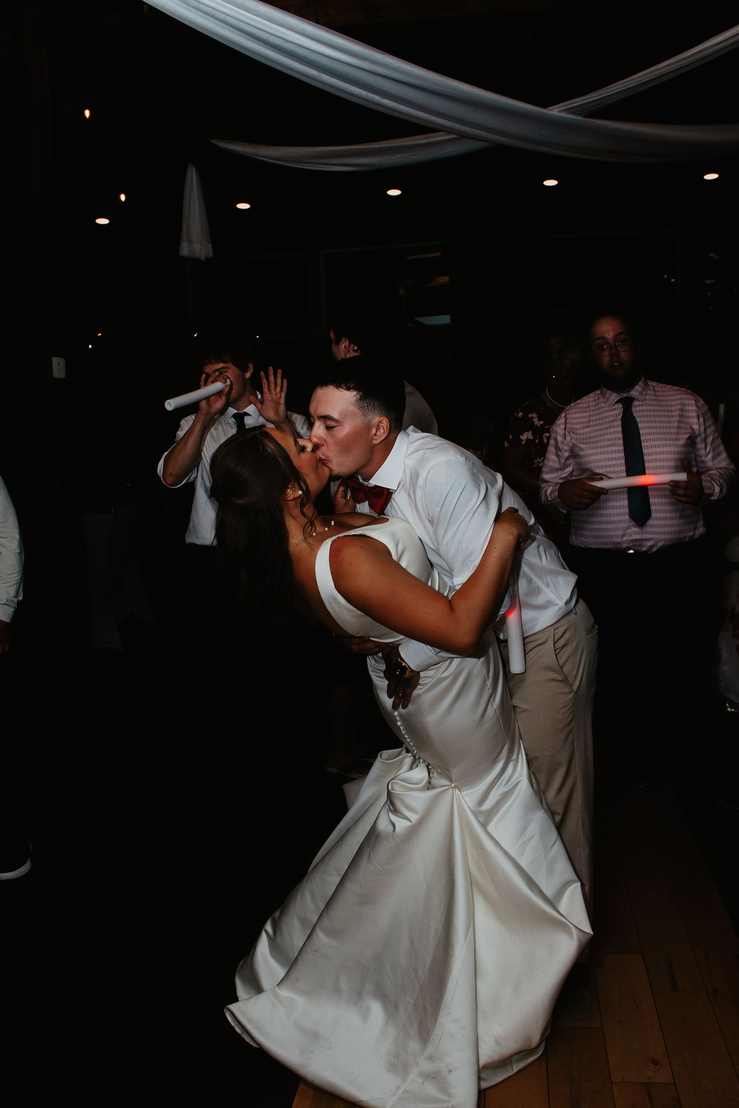 Bride and groom share a romantic dip kiss on the wedding reception dance floor surrounded by guests holding glow sticks on Film in PA