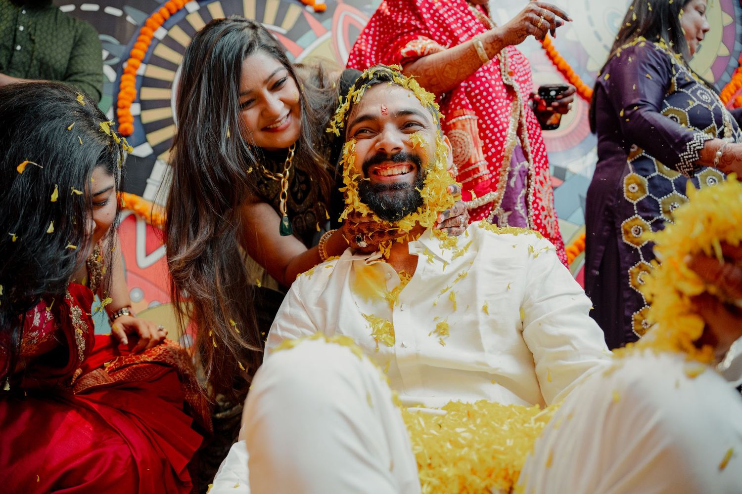 Joyful groom covered in yellow flowers during Indian wedding haldi ceremony surrounded by smiling women in Philadelphia PA