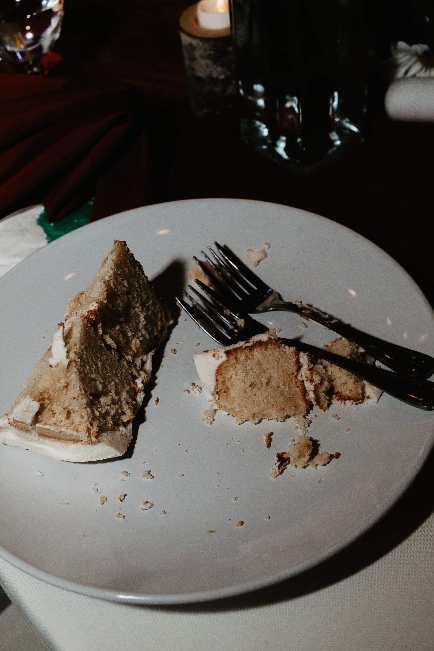 Partially eaten slice of wedding cake with crumbs on a white plate, with a fork and knife at a dimly lit restaurant. Captured on Film in PA