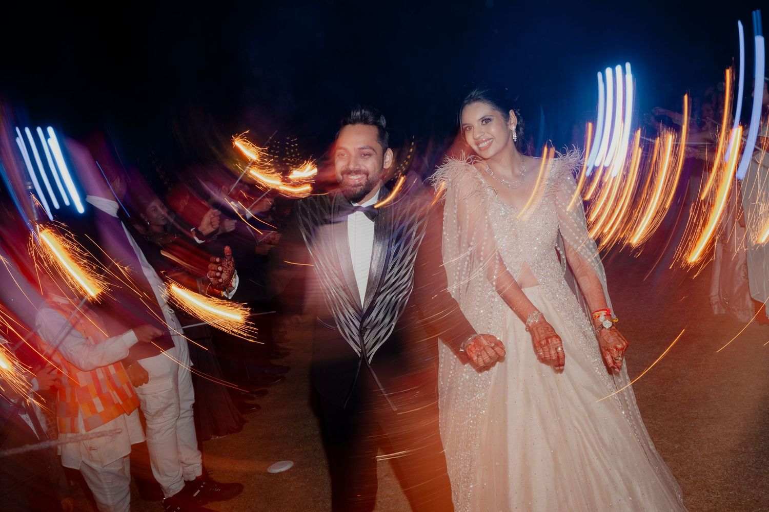 Bride and groom holding hands at night wedding celebration with colorful light trails and sparklers in background in Philly