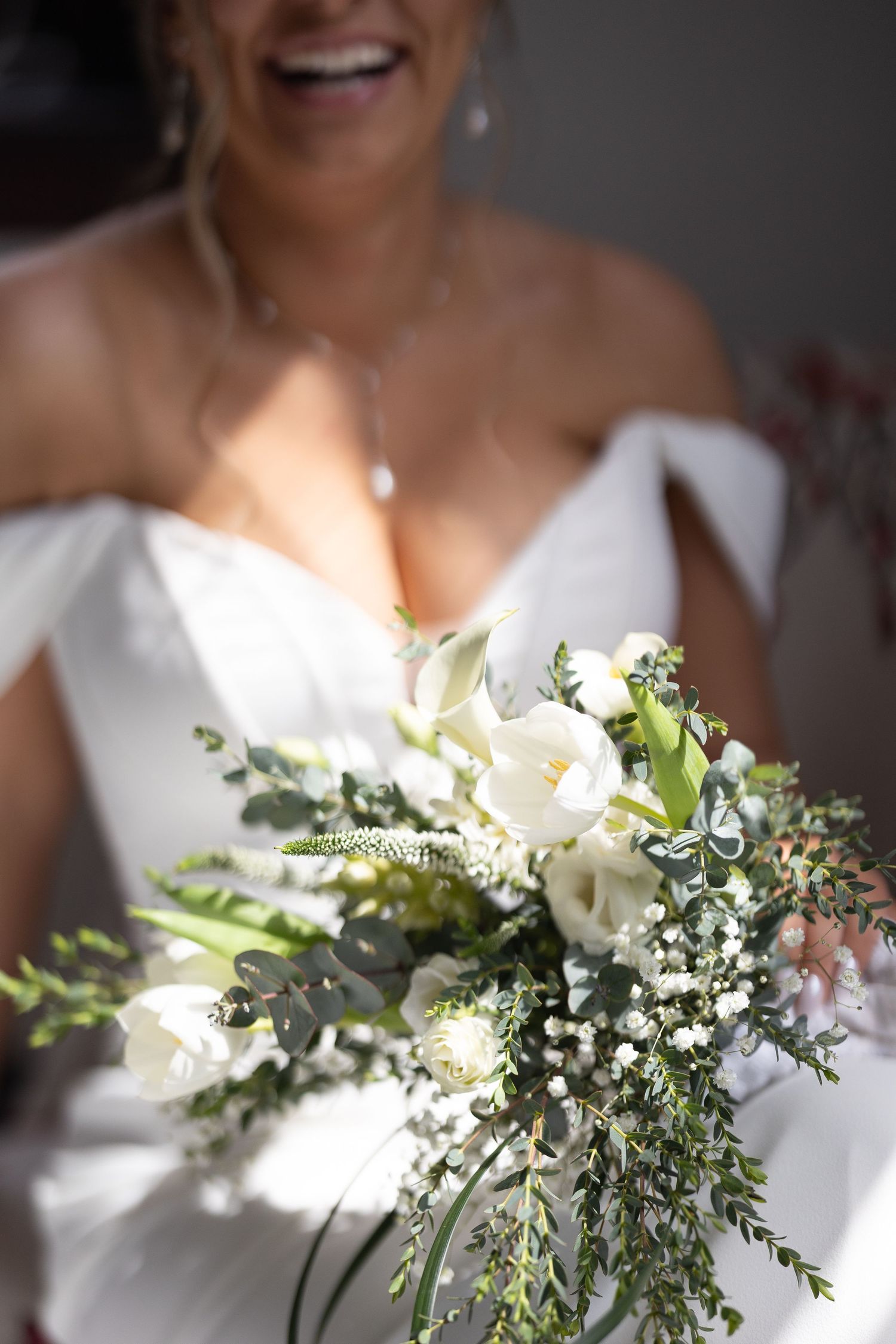 Smiling bride in off-shoulder white gown holding lush white and greenery wedding bouquet. Luxury Wedding Photography in Pennsylvania