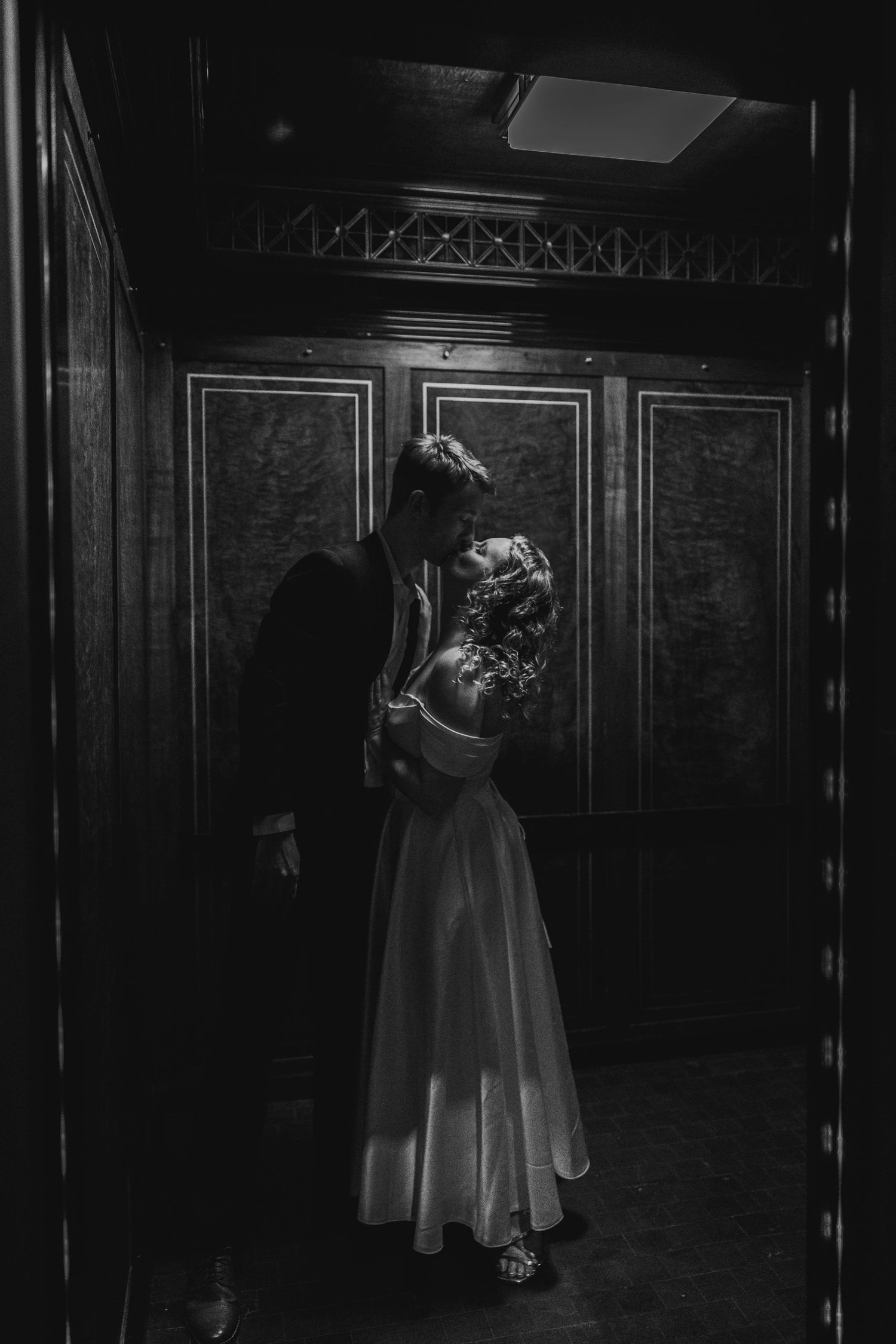Black and white film photo of a bride and groom sharing a romantic moment in an ornate elevator. Film wedding photography