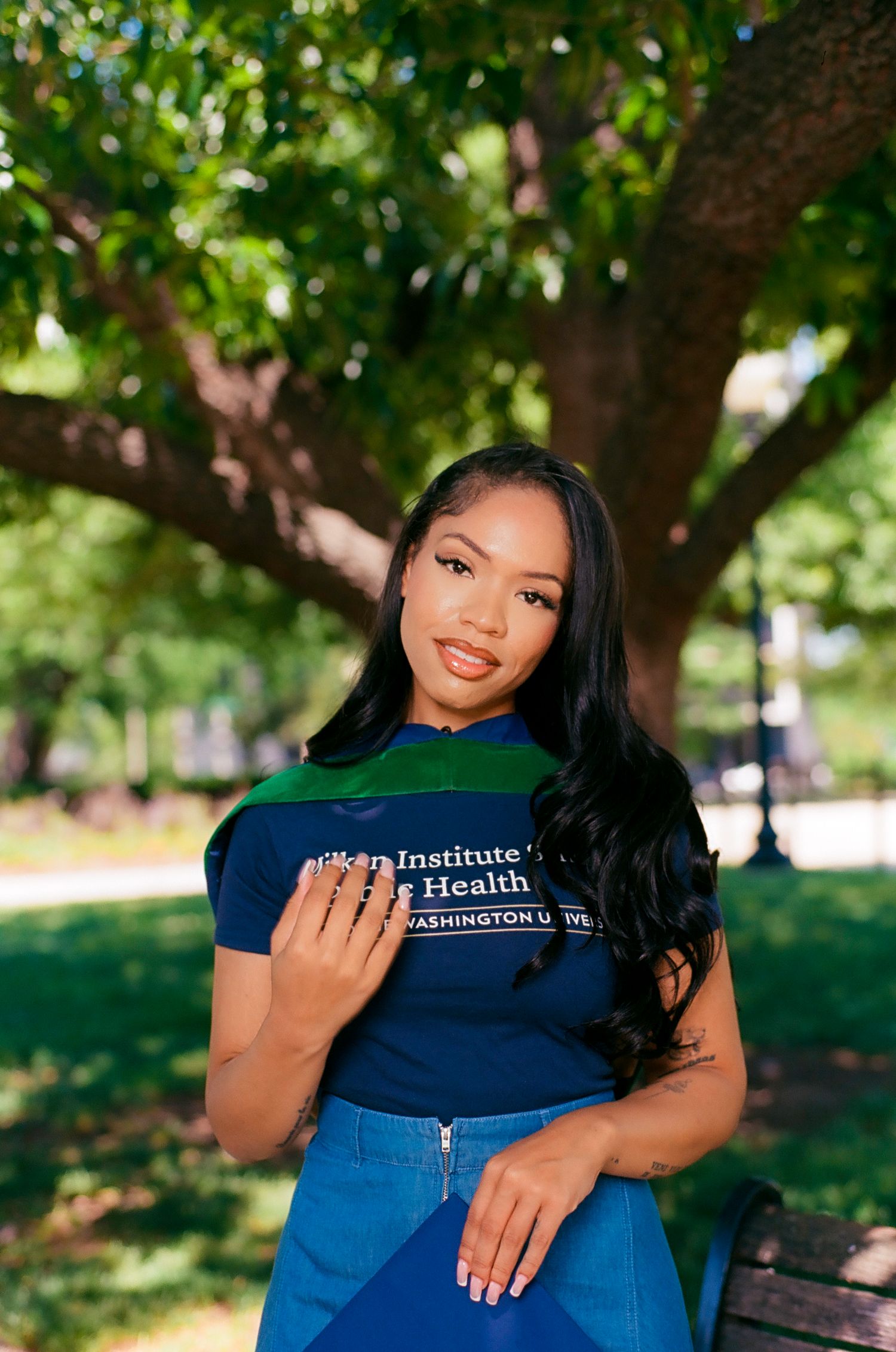 Young woman in Washington University Health Institute shirt poses outdoors near a tree in a sunny park.