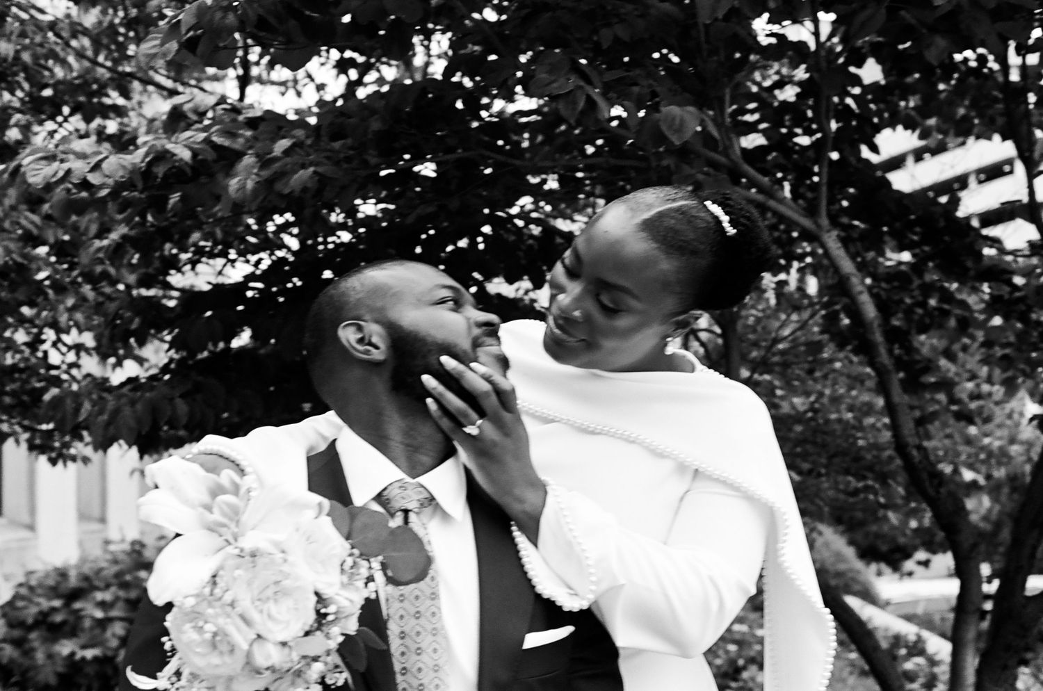 Black and white wedding photo of a couple, bride tenderly touching groom's face outdoors.