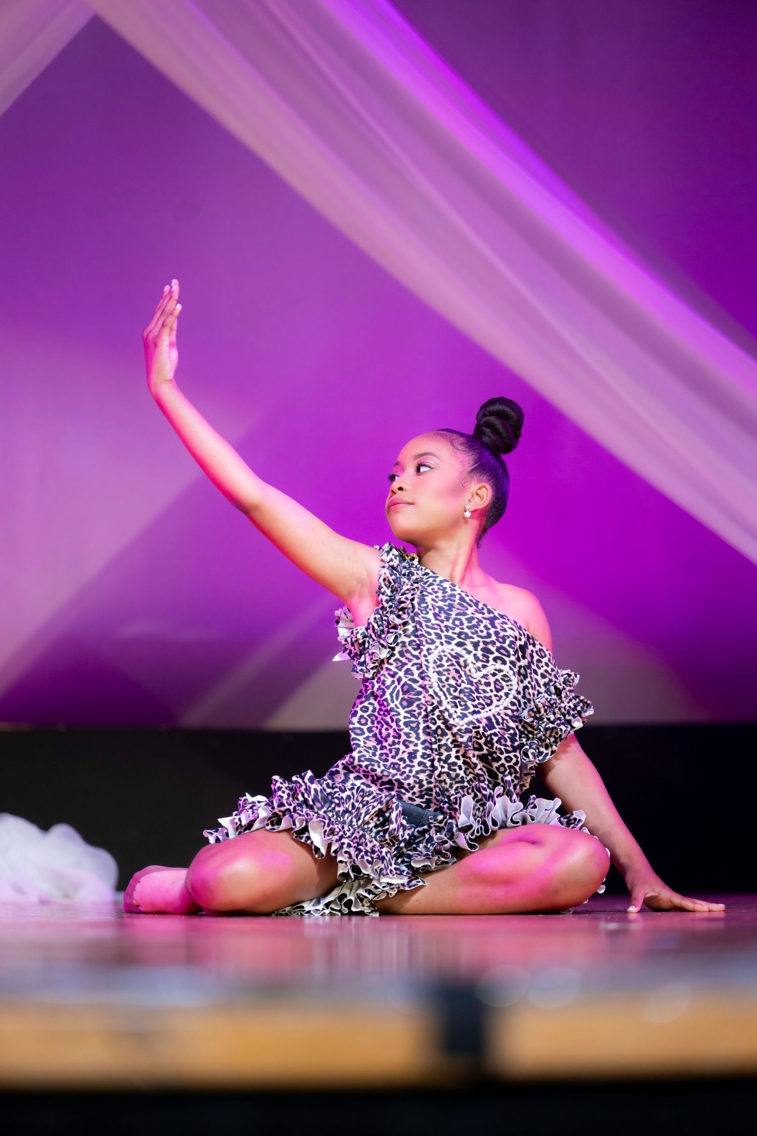 Young dancer in leopard print costume performs graceful floor routine on stage with purple lighting.