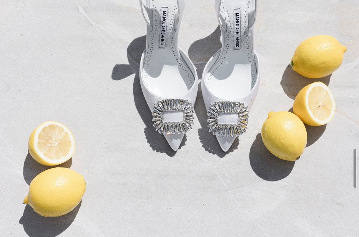 Minimalist still life of white shoes and fresh lemons arranged on light background.
