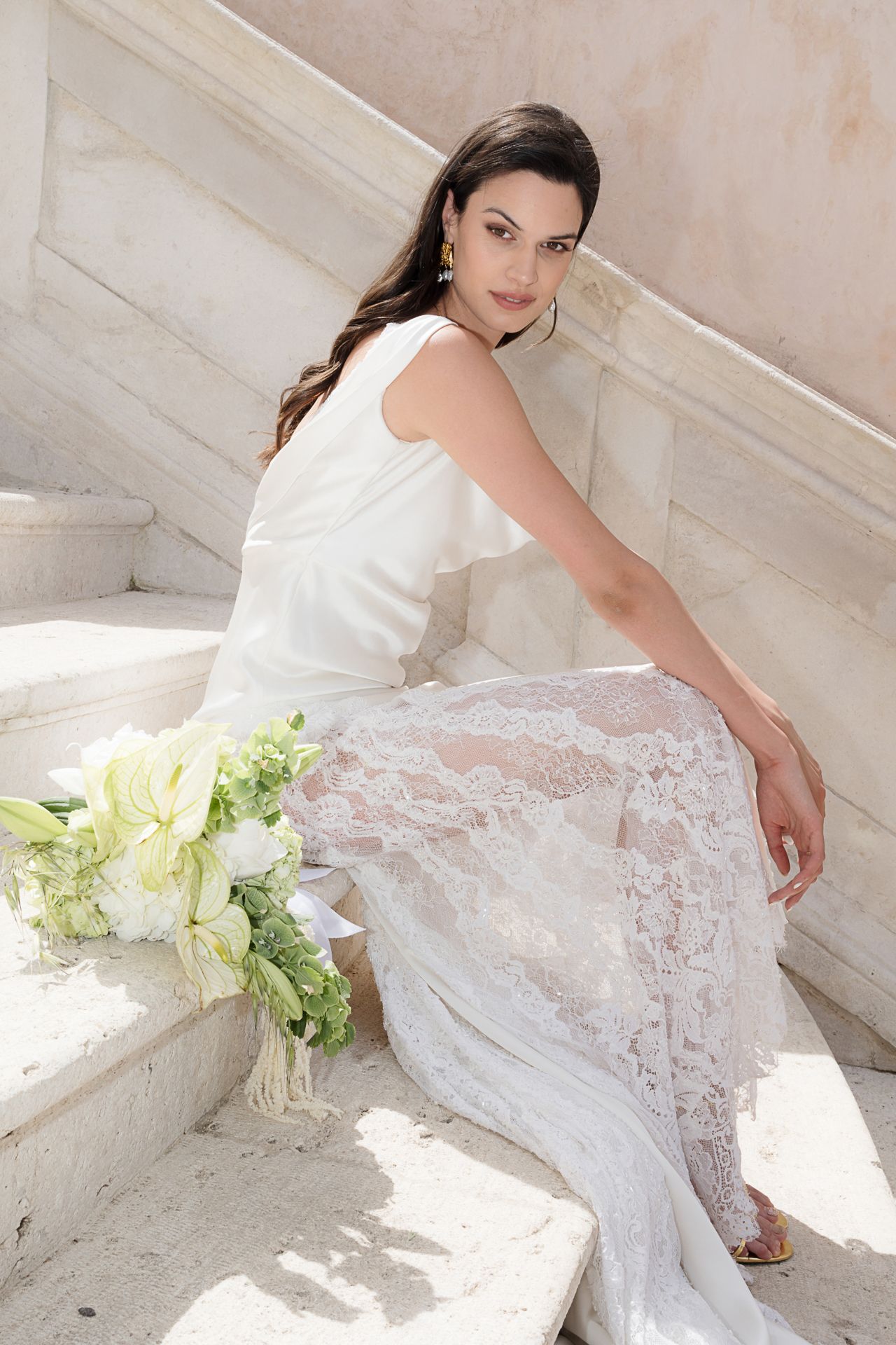 Elegant bridal portrait on marble stairs with white lace dress and floral bouquet.