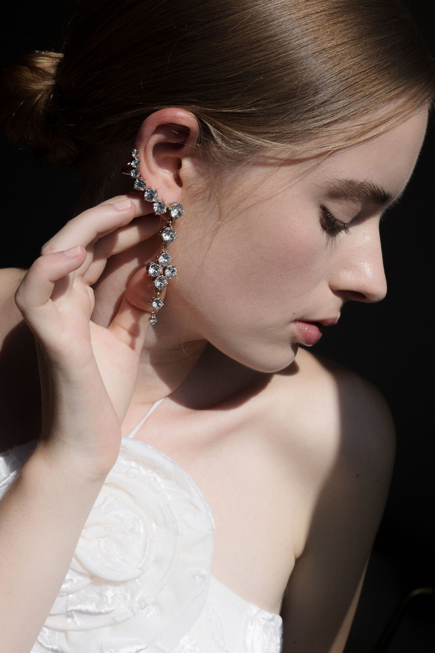 Elegant crystal drop earring sparkles in dramatic lighting against white bridal gown and soft skin.