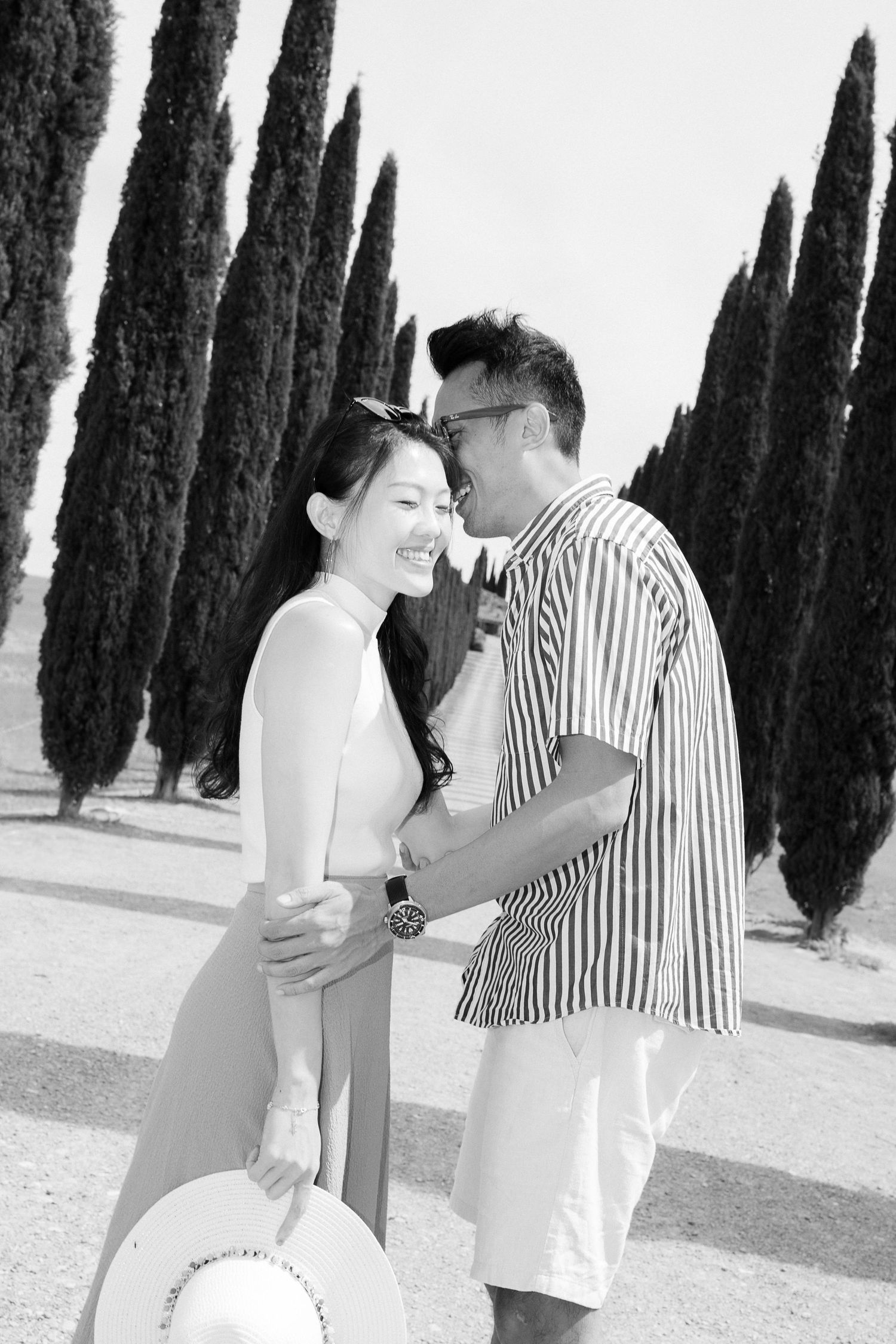 A romantic couple shares intimate moments among tall cypress trees in a garden setting.