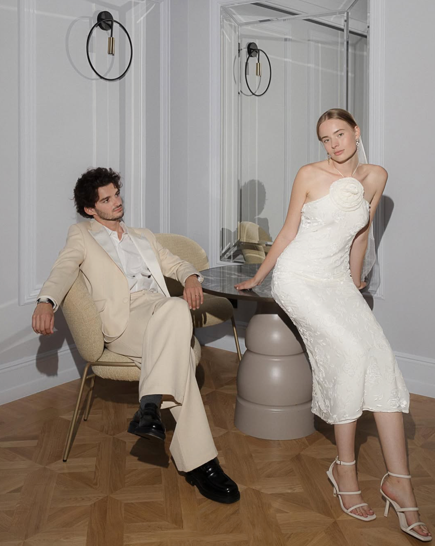 Modern wedding fashion shoot with couple posing casually on contemporary grey chairs.