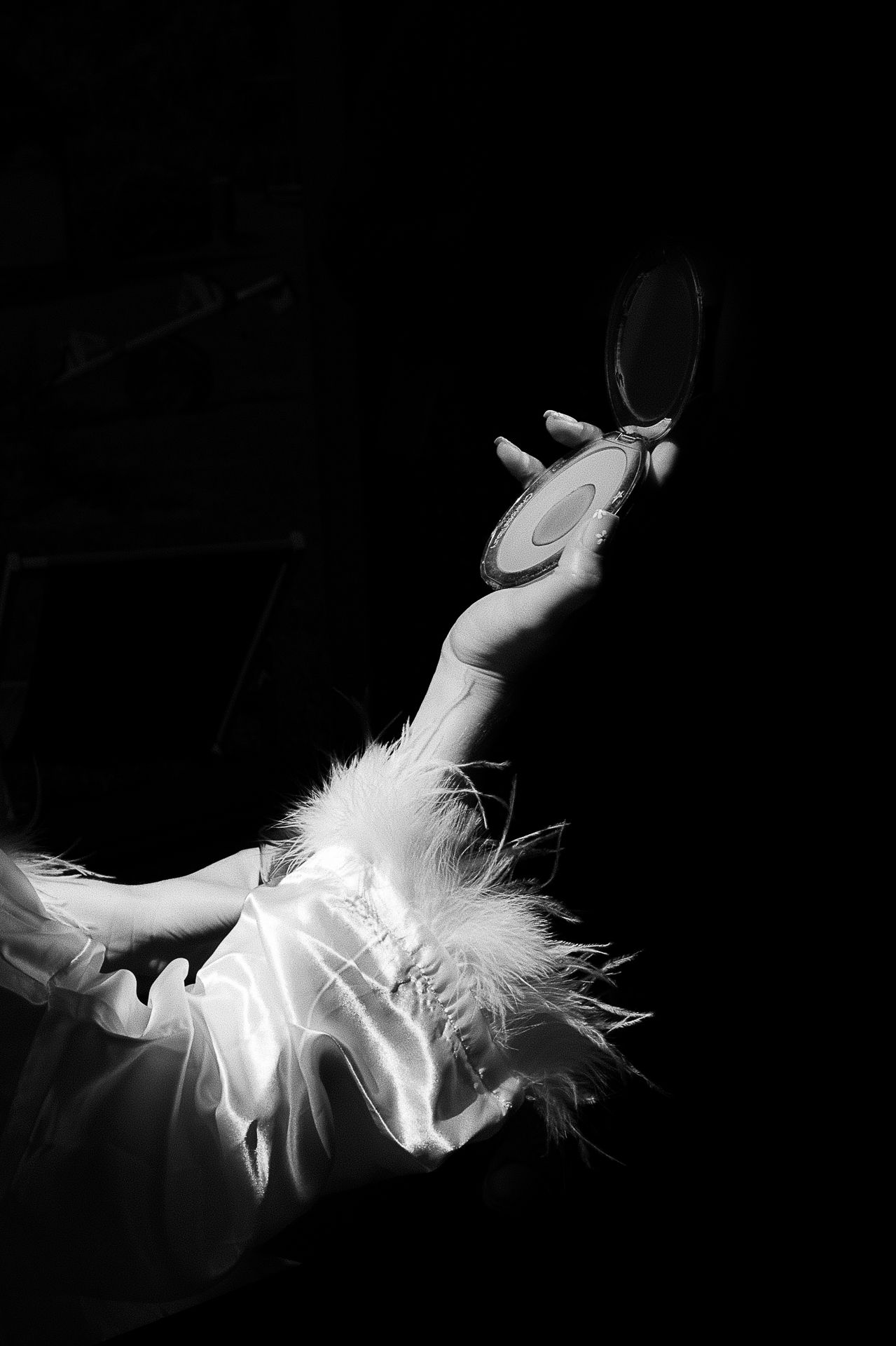 Dramatic black and white photo of ballet dancer holding compact mirror.