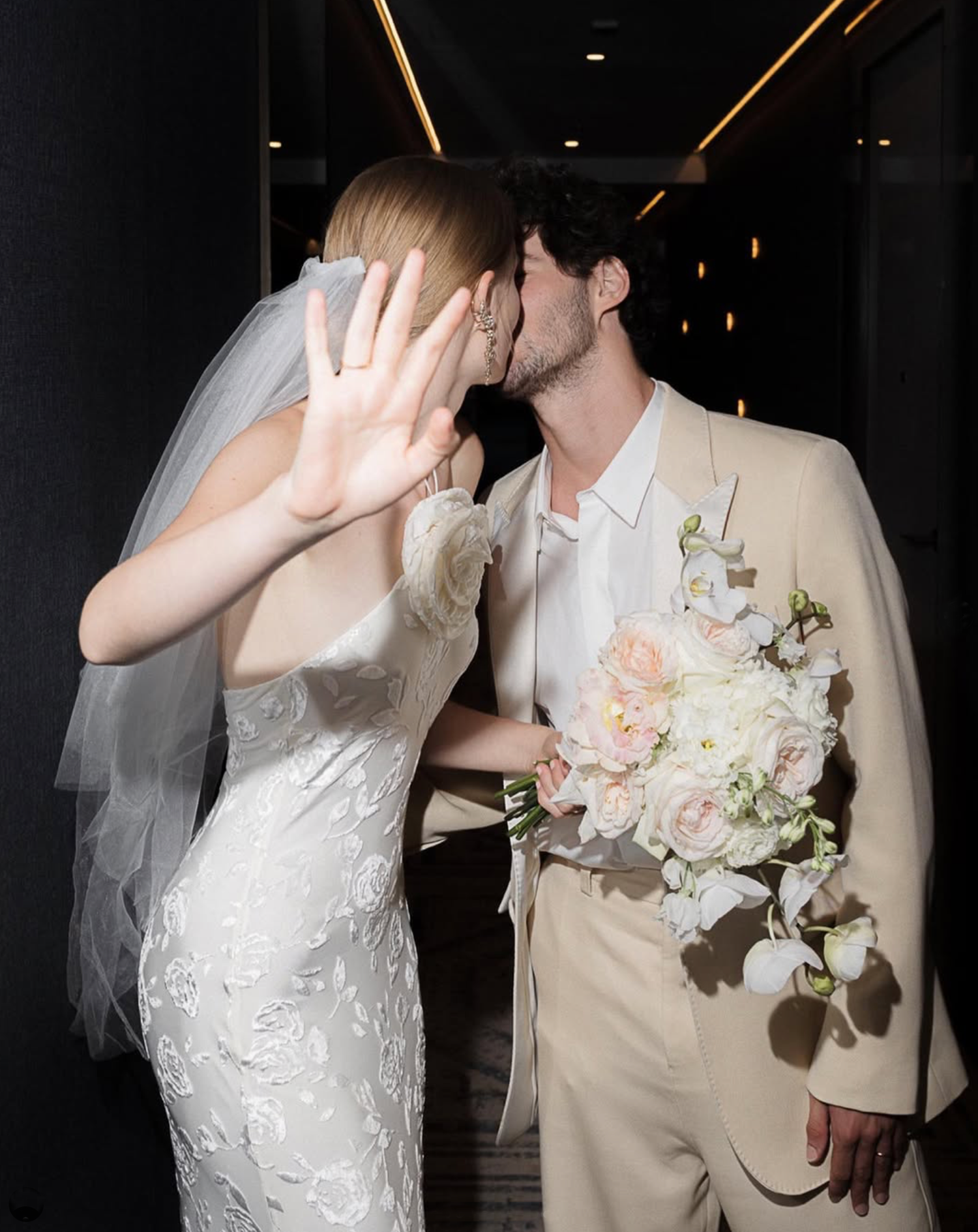 Bride and groom in elegant wedding attire share a playful moment waving at the camera.