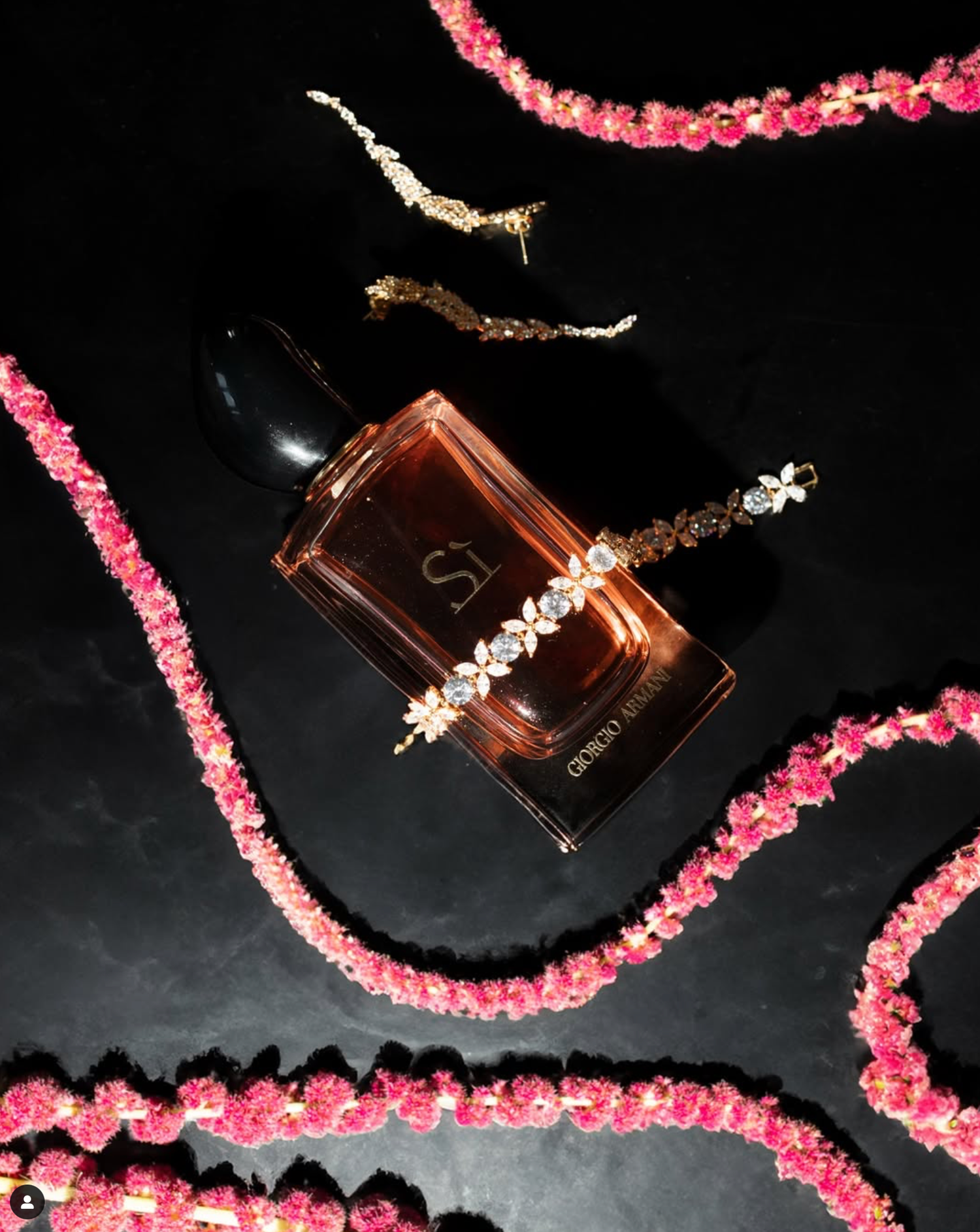 Luxury perfume bottle surrounded by pink crystal beads on dark reflective surface.