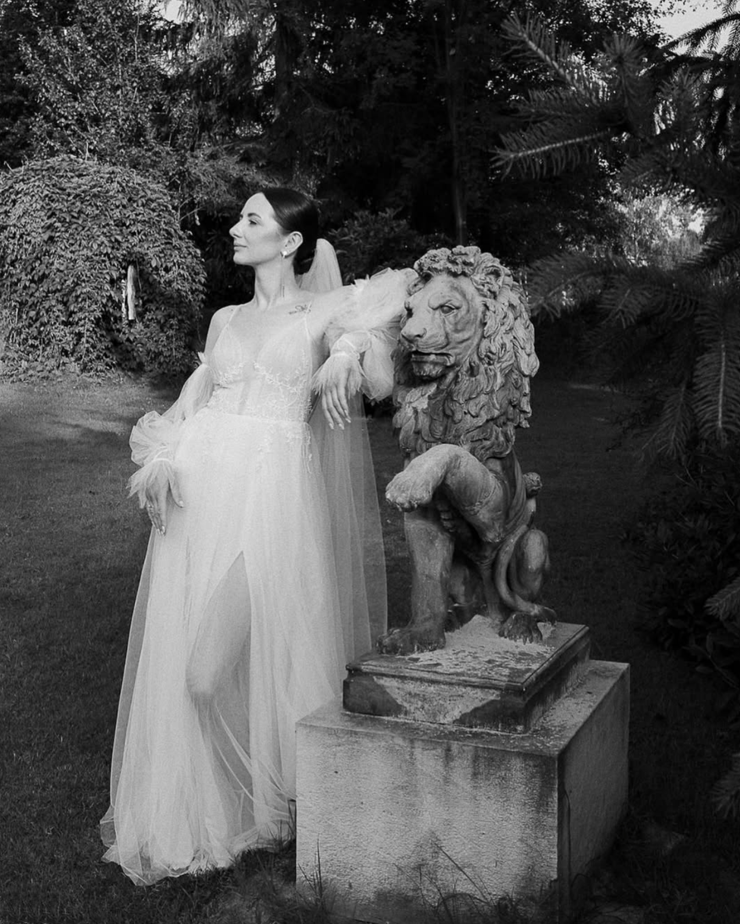 Ethereal garden scene with flowing white dress near classical stone statuary in black and white.