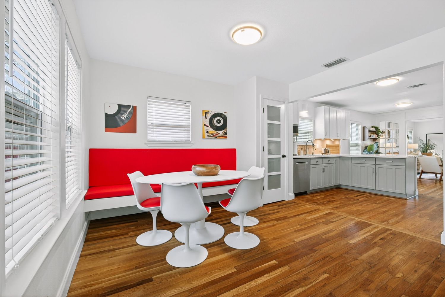 Modern open concept office space with hardwood floors, white walls, and natural light streaming through horizontal blinds.