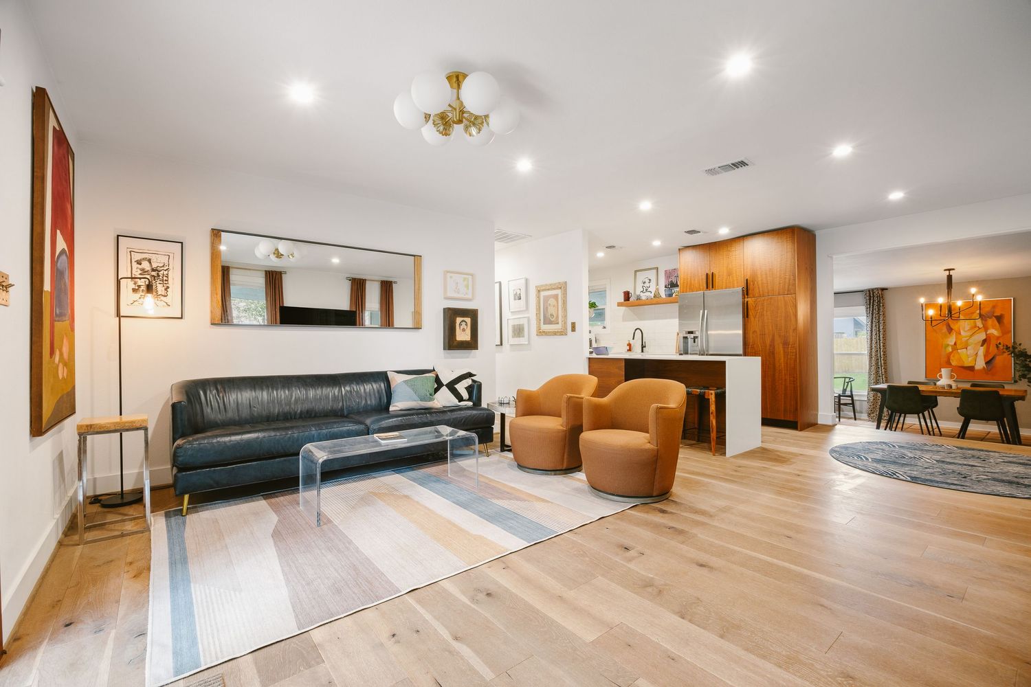 Modern living room with leather sofa, hardwood floors, striped rug, and open-concept kitchen featuring warm wood cabinetry.