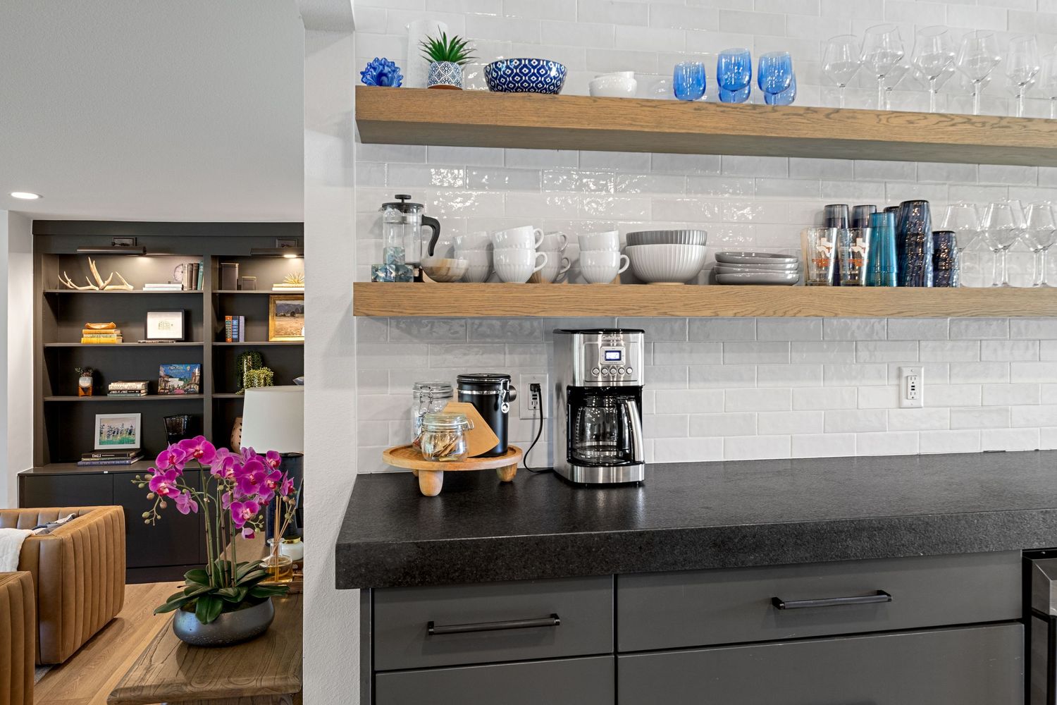 Modern kitchen coffee bar with open wood shelves, black countertop, coffee maker, and white subway tile backsplash.