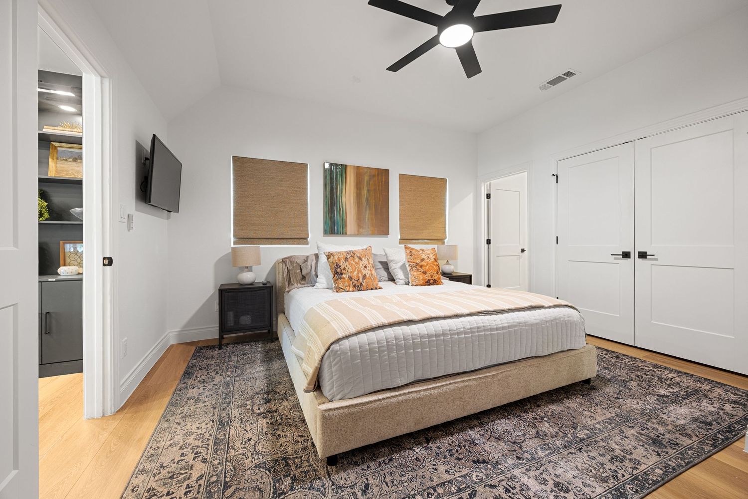 Spacious master bedroom with ceiling fan, king bed, patterned rug, and wall-mounted TV on hardwood floors.