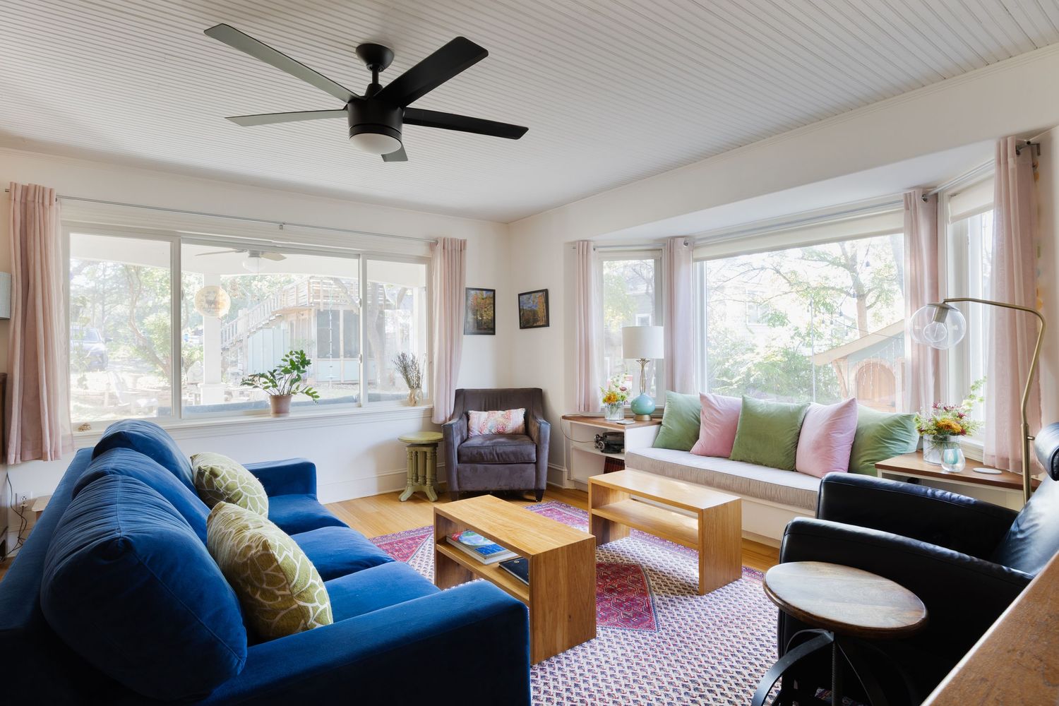 Spacious living area with ceiling fan, blue couch, and large windows overlooking greenery.