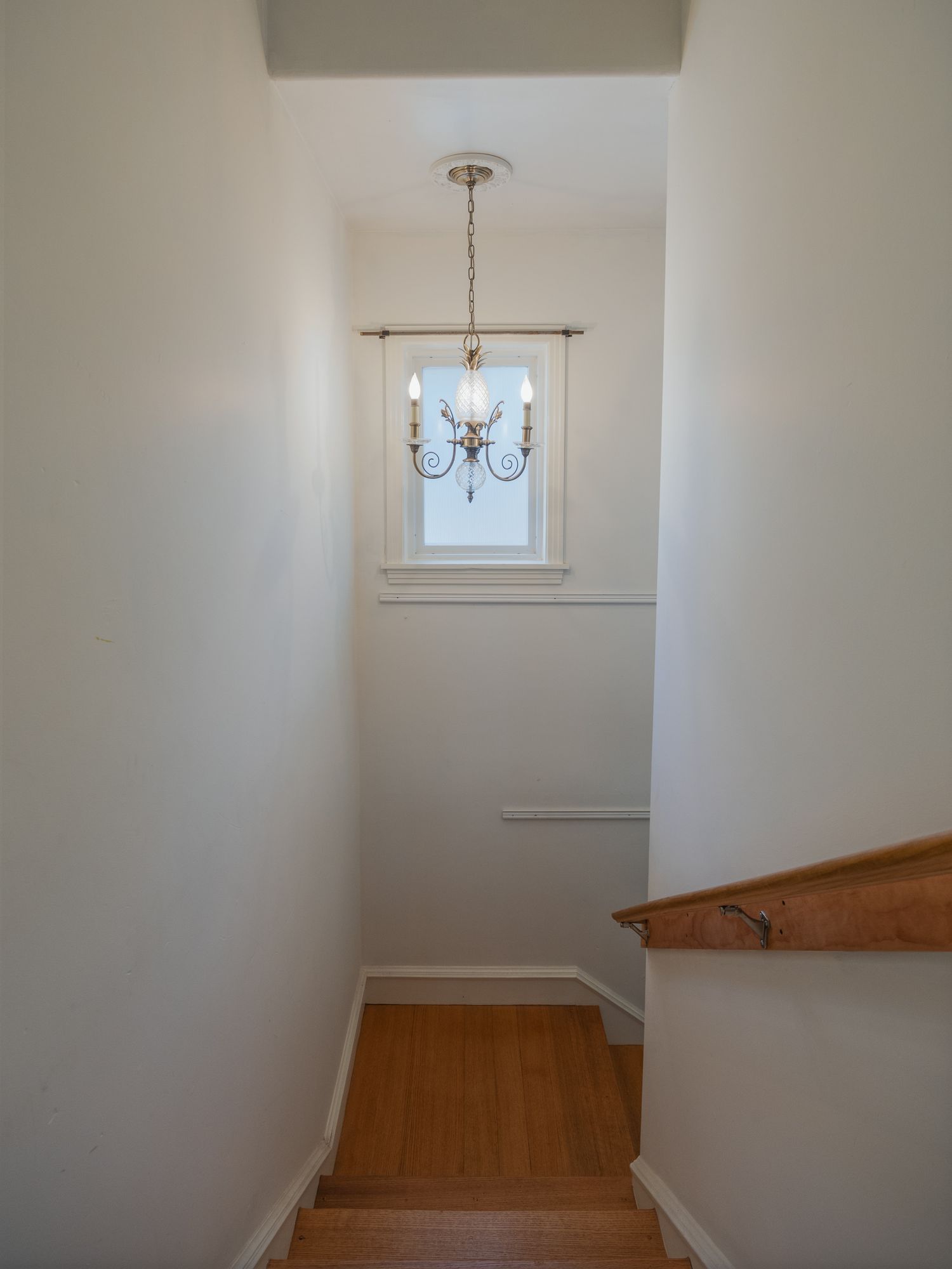 White stairwell hallway with chandelier and wooden handrail.