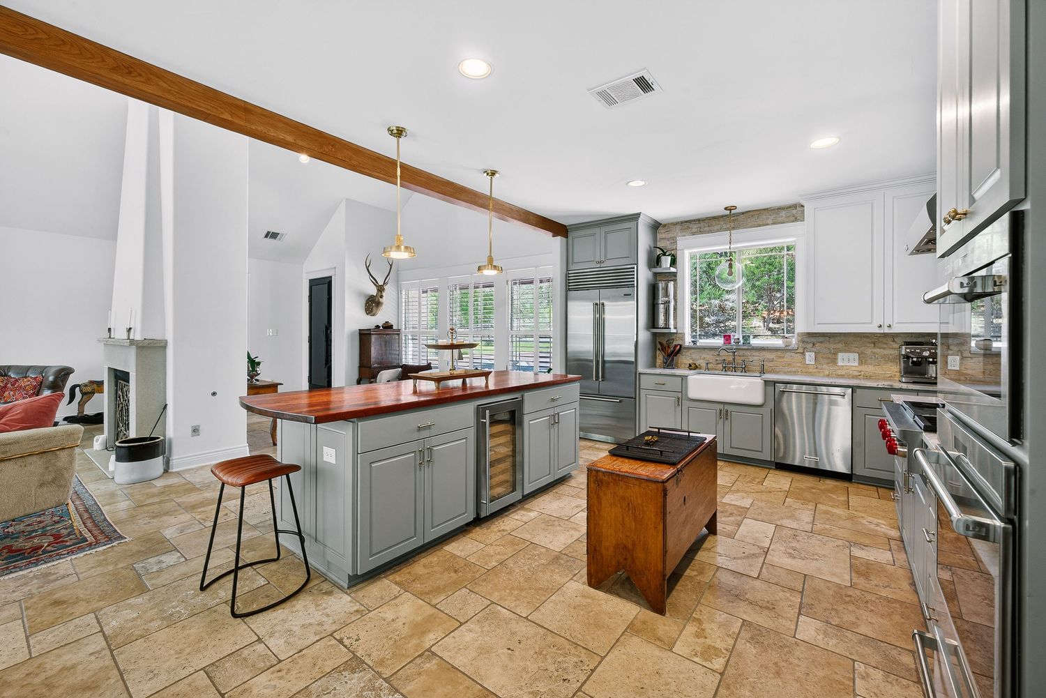 Spacious kitchen with gray cabinets, butcher block island, wine cooler, pendant lights, and stone tile flooring.