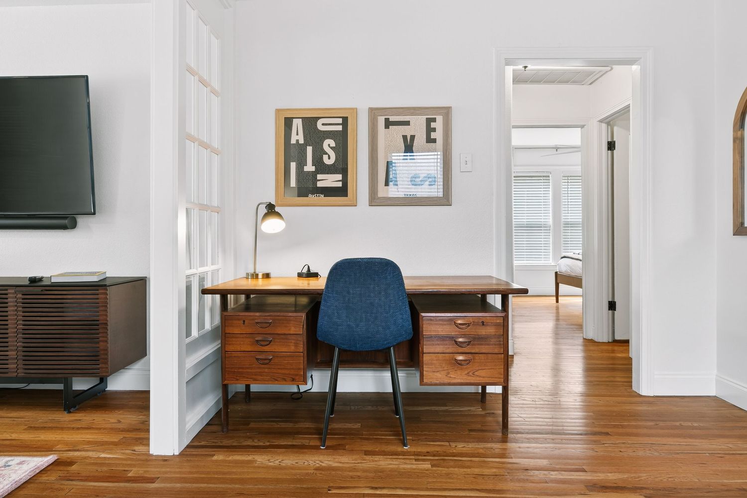 Minimalist white hallway interior with hardwood flooring and vintage wooden furniture pieces against the walls.