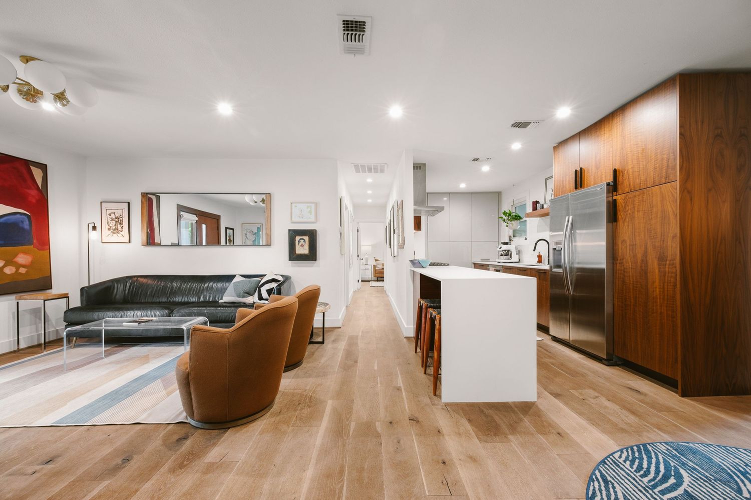 Modern open-concept living space with hardwood floors, leather seating, white kitchen island, and walnut cabinetry.