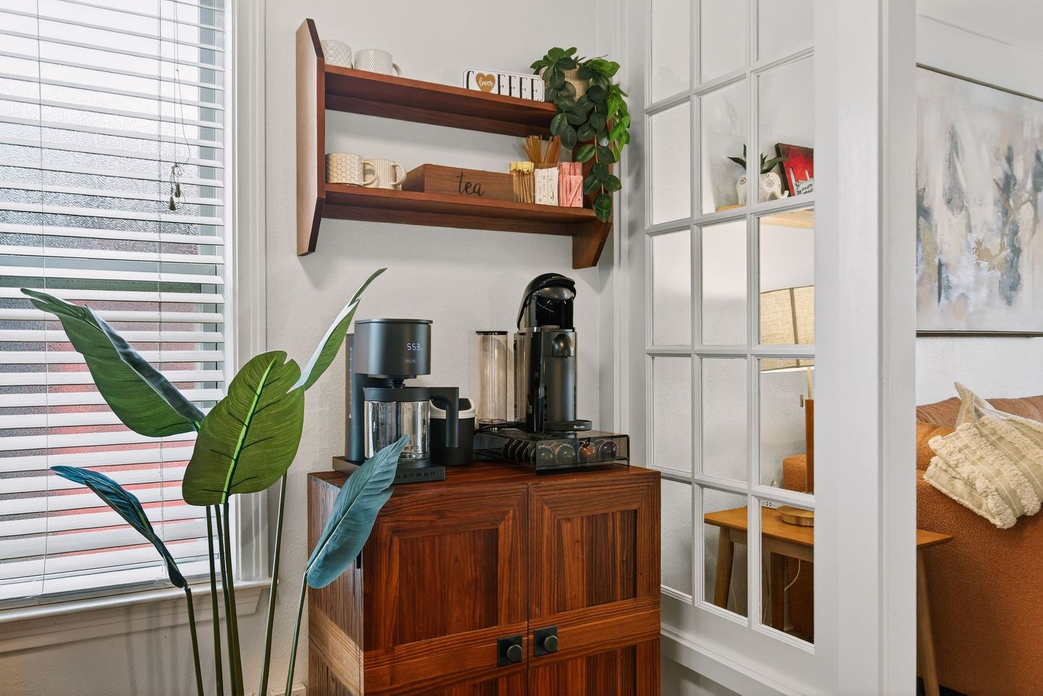 A bright modern living room features white walls, houseplants, wooden furniture and natural lighting from windows.