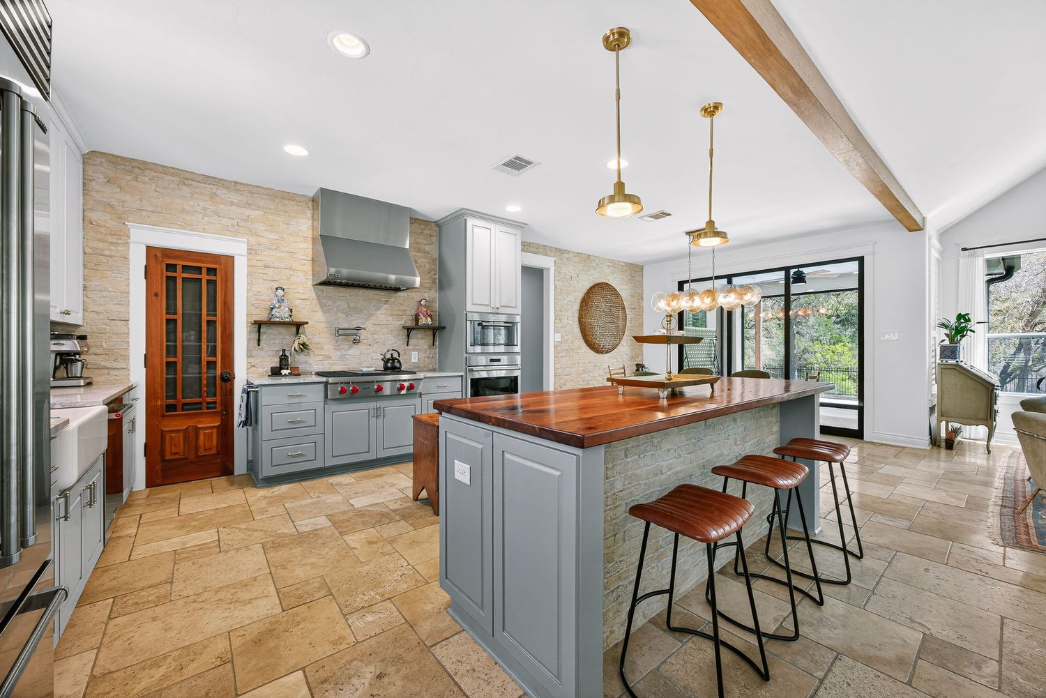 Spacious kitchen with gray cabinets, butcher block island, pendant lights, stone tile floors, and stainless steel appliances.