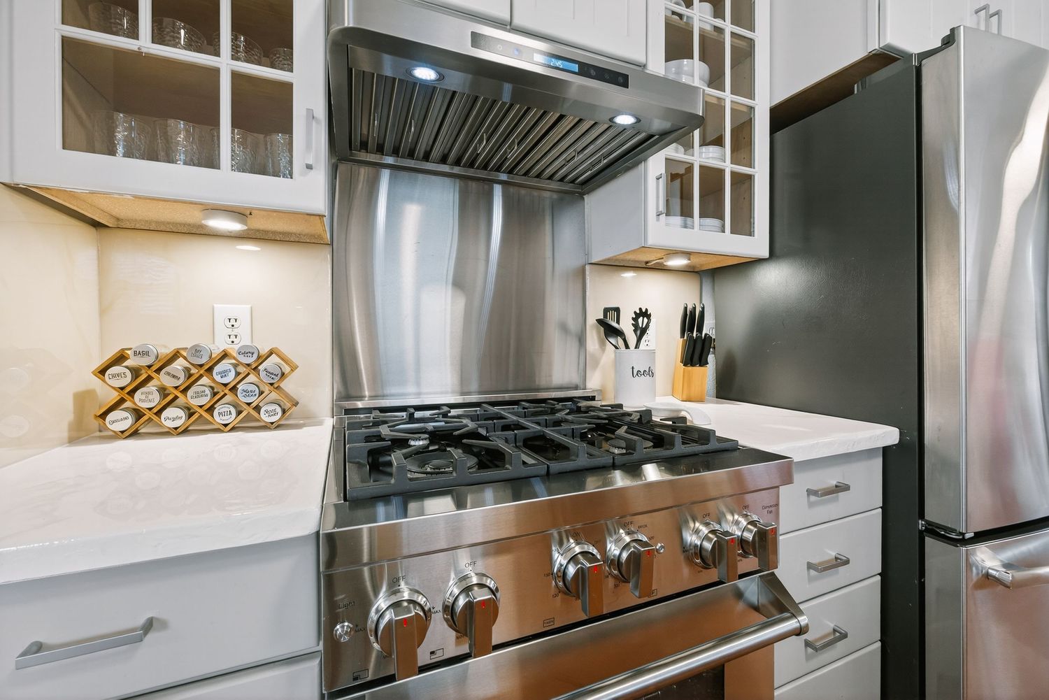 Modern white kitchen with stainless steel appliances features gas range, sleek cabinets and glass tile backsplash.