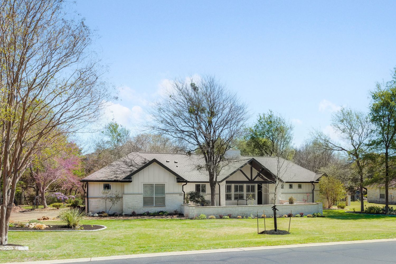 Spacious ranch-style home with white exterior, lush green lawn, and mature trees under a bright blue sky.