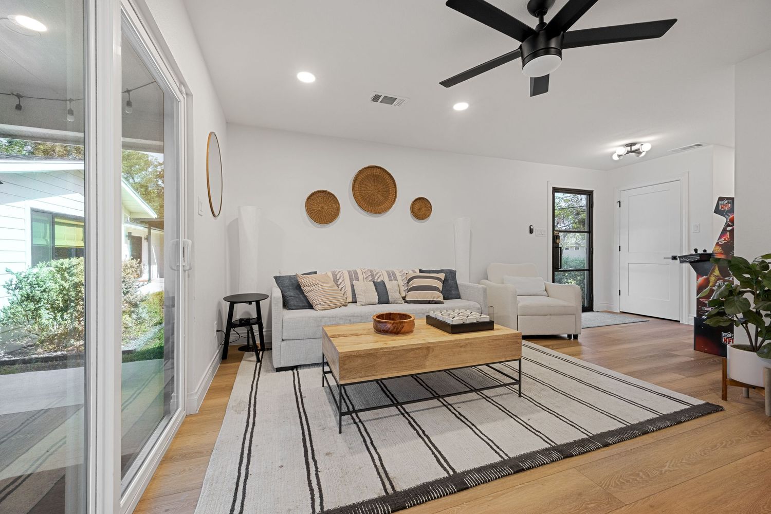 Bright living room with white sofa, striped rug, wood coffee table, ceiling fan, and large windows.