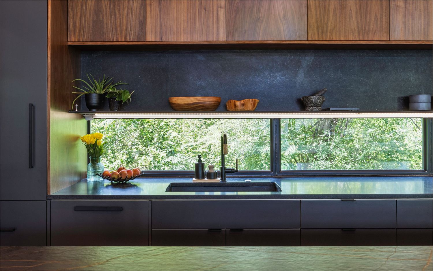 Modern kitchen design featuring a sleek horizontal window backsplash with garden views and dark wood cabinetry.
