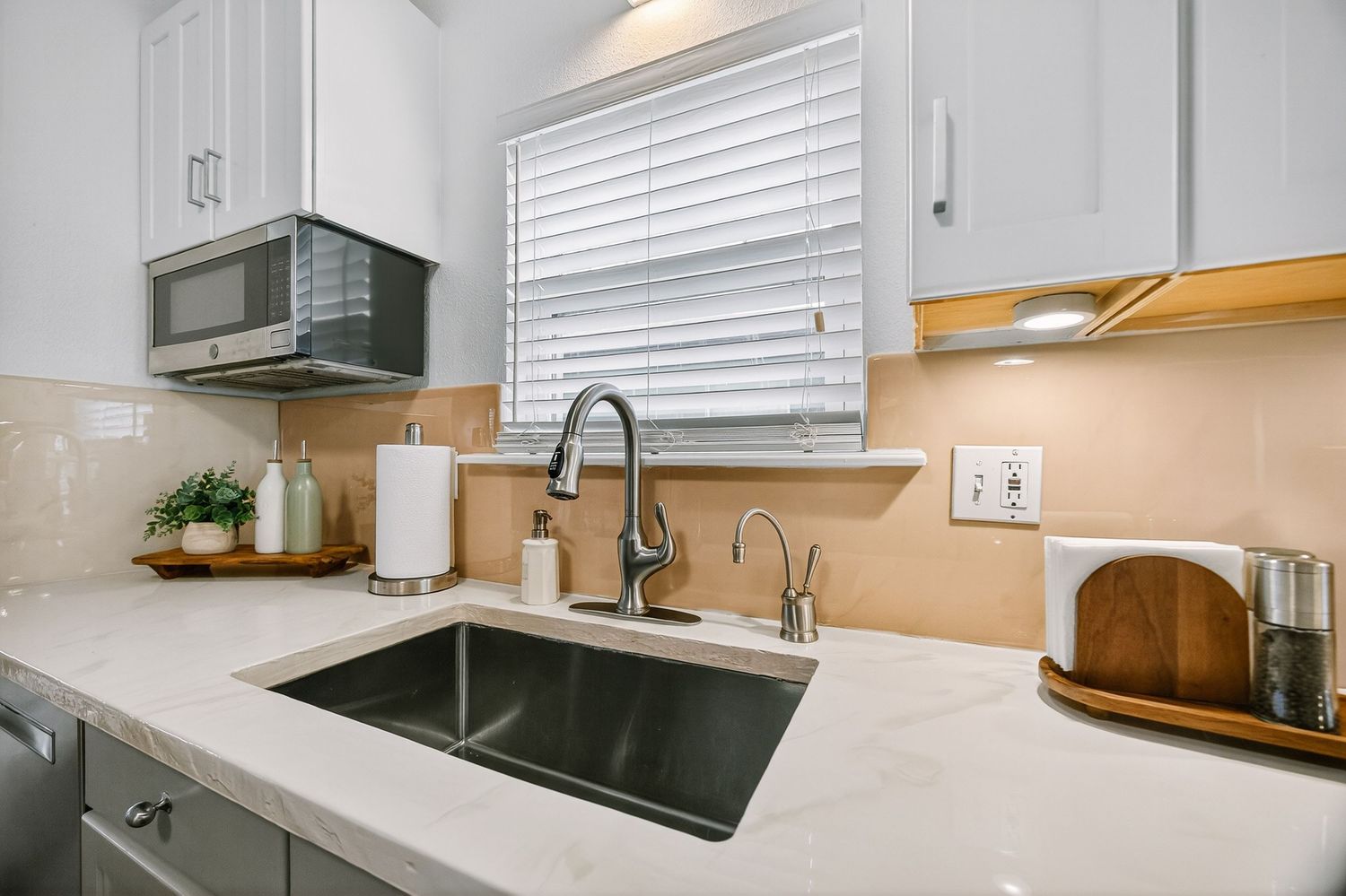 Modern kitchen with white cabinets, quartz countertops, stainless steel appliances and hardwood floors.