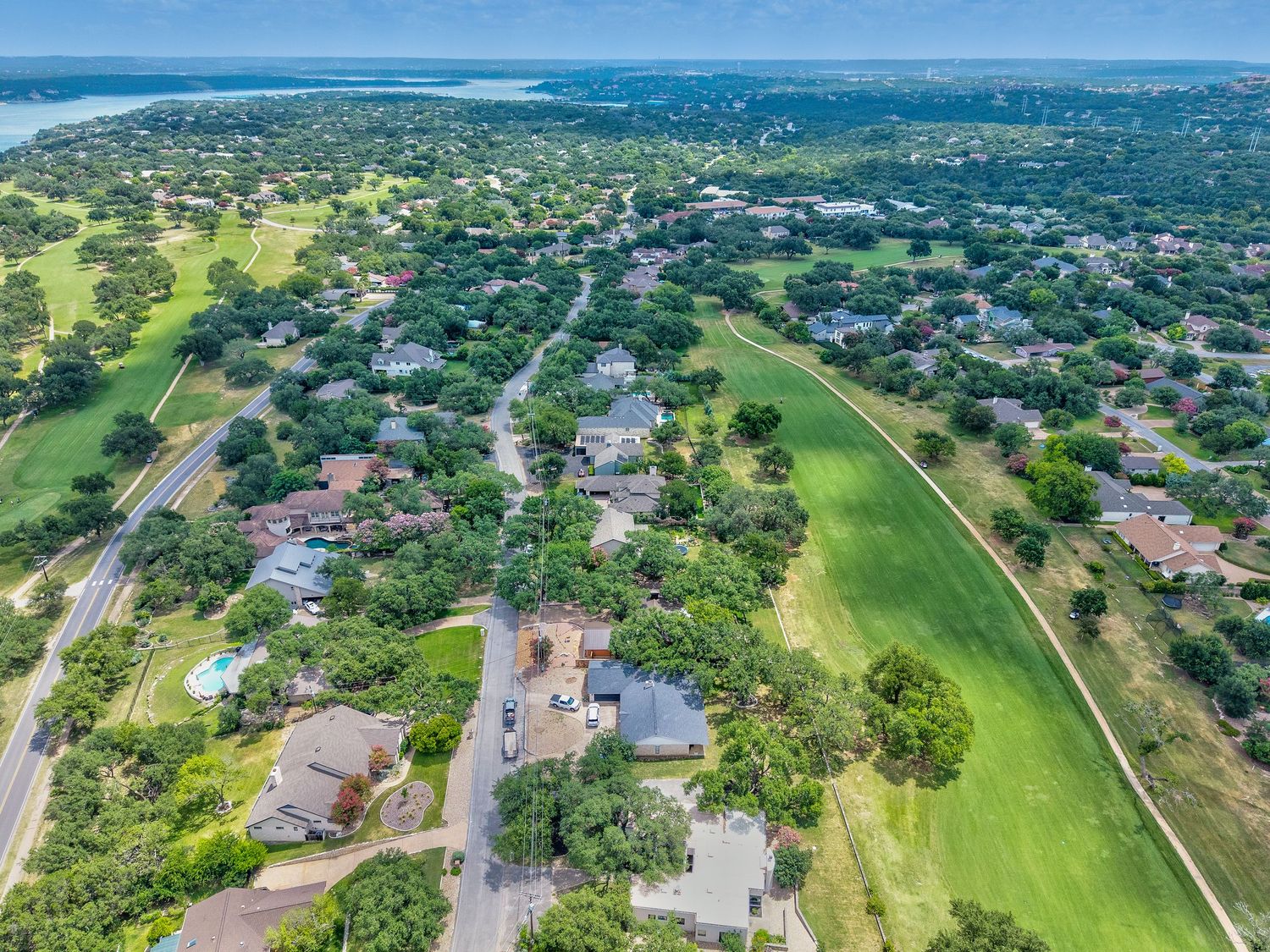 Aerial view of a residential neighborhood with tree-lined streets, homes, a green golf fairway, and a lake in the distance.