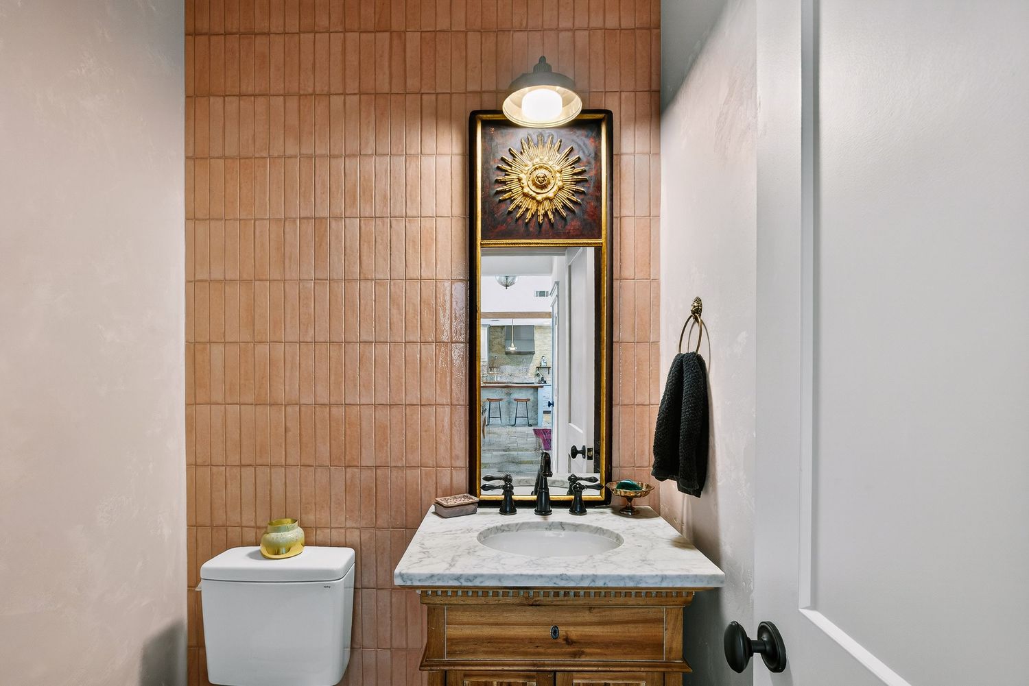 Elegant powder room with terracotta tile wall, ornate wood vanity, marble countertop, and decorative sun mirror.