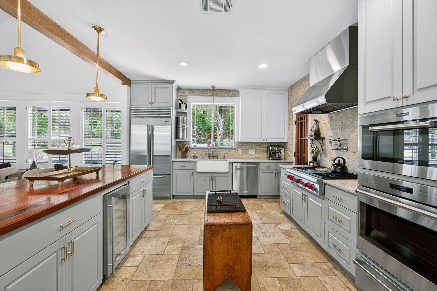 Modern kitchen featuring gray cabinets, professional range, stainless appliances, butcher block counters, and gold pendant lights.