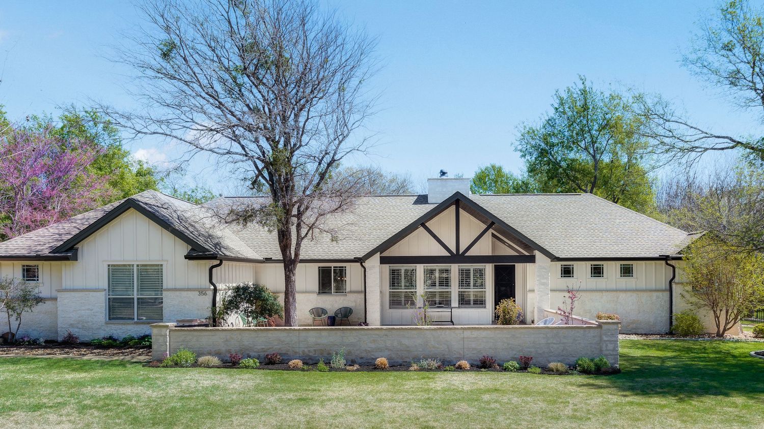 Ranch-style home with Tudor accents, white exterior, manicured lawn, and mature trees in a suburban spring setting.