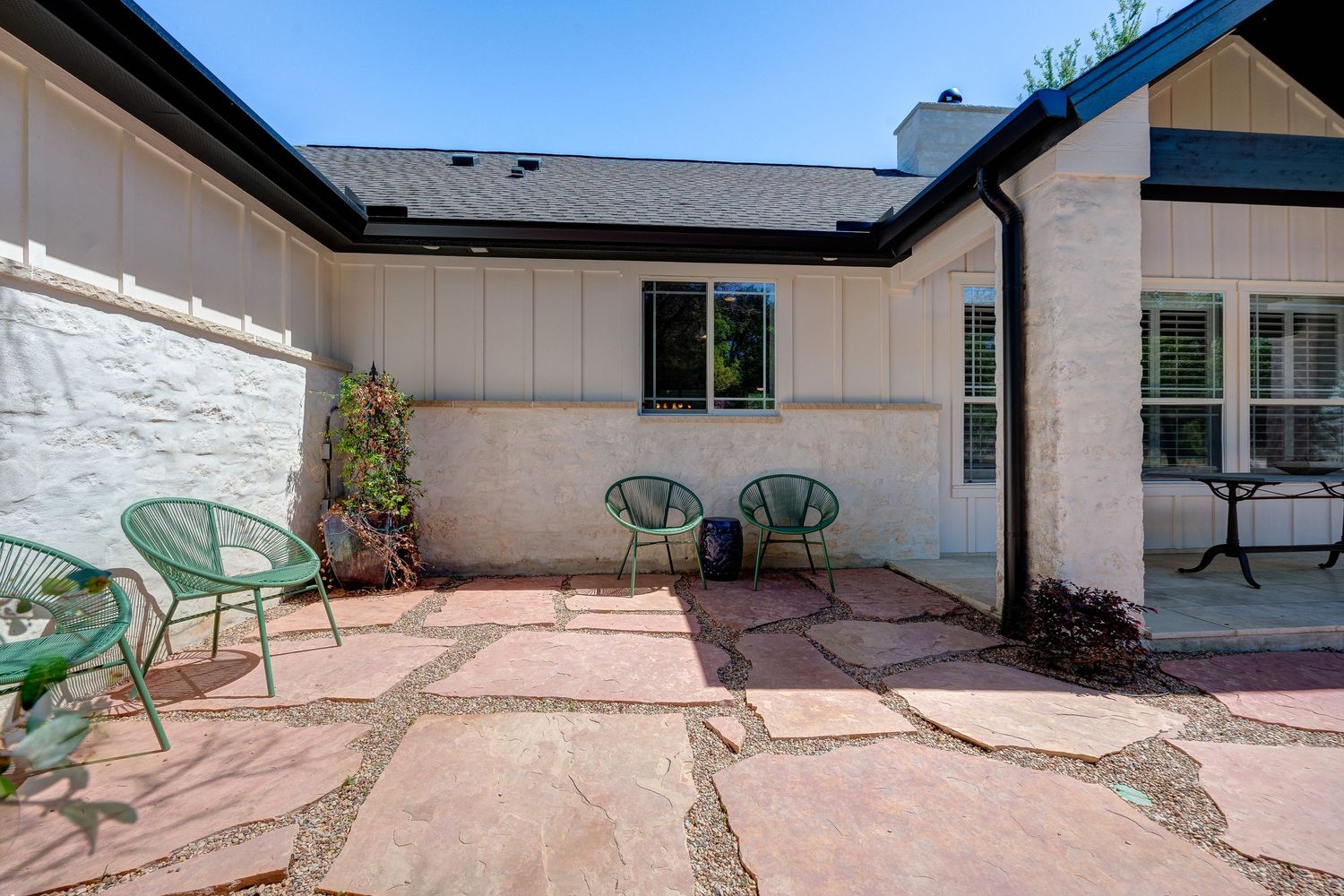 Cozy patio with flagstone flooring, green chairs, and a stucco home exterior surrounded by lush landscaping.