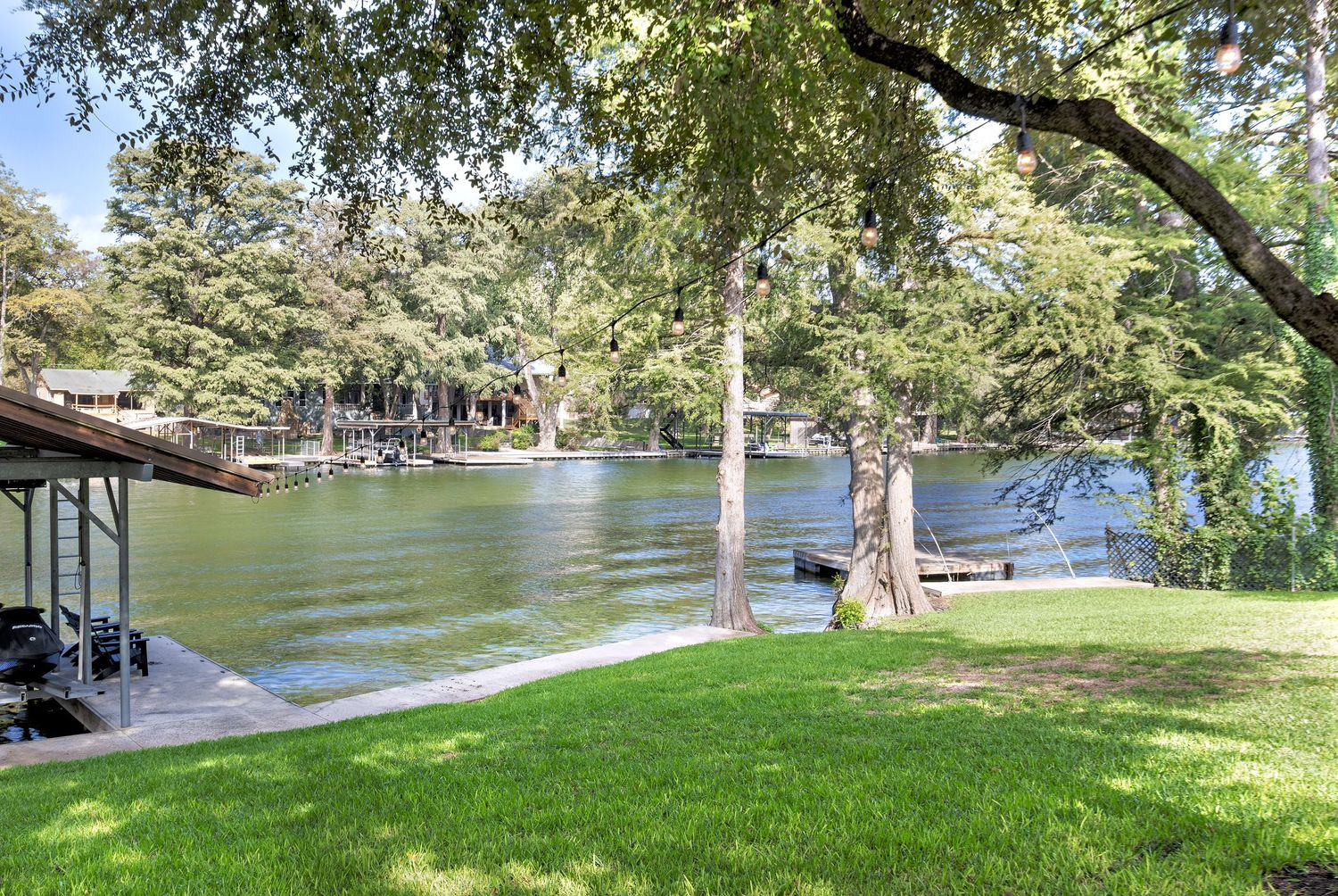 Peaceful lakefront backyard with lush green lawn, mature oak trees, private dock, and calm water views.