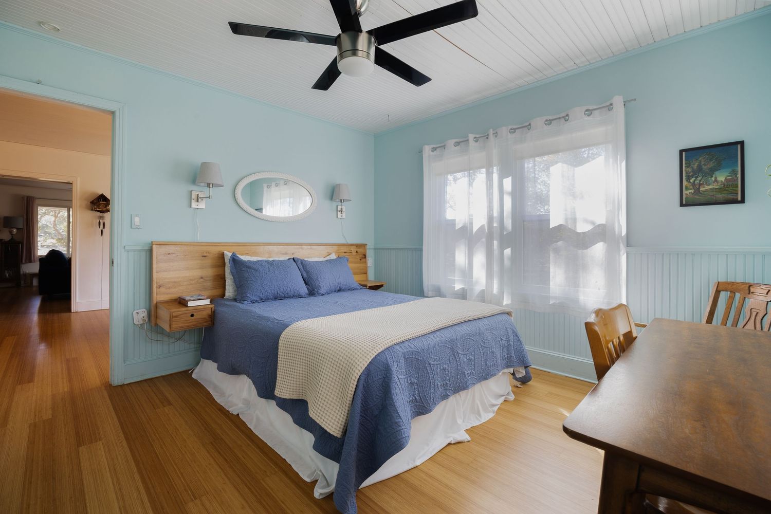 Spacious bedroom with blue walls, wooden furniture, and navy bedding under a black ceiling fan.