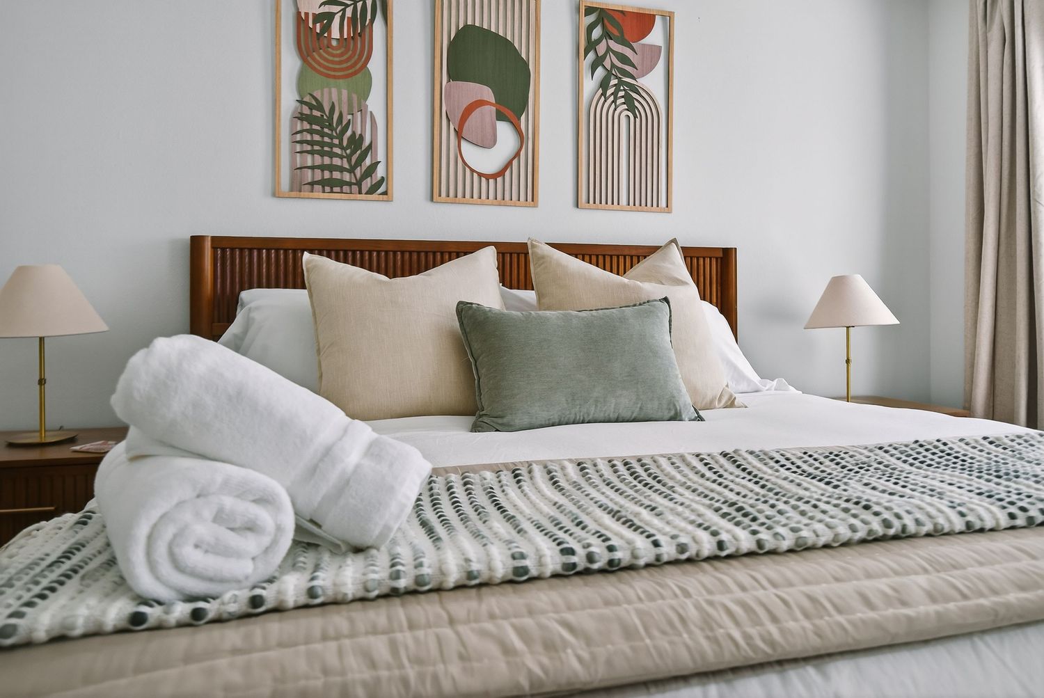Modern bedroom with wooden headboard, botanical wall art, neutral bedding, and decorative throw blankets.